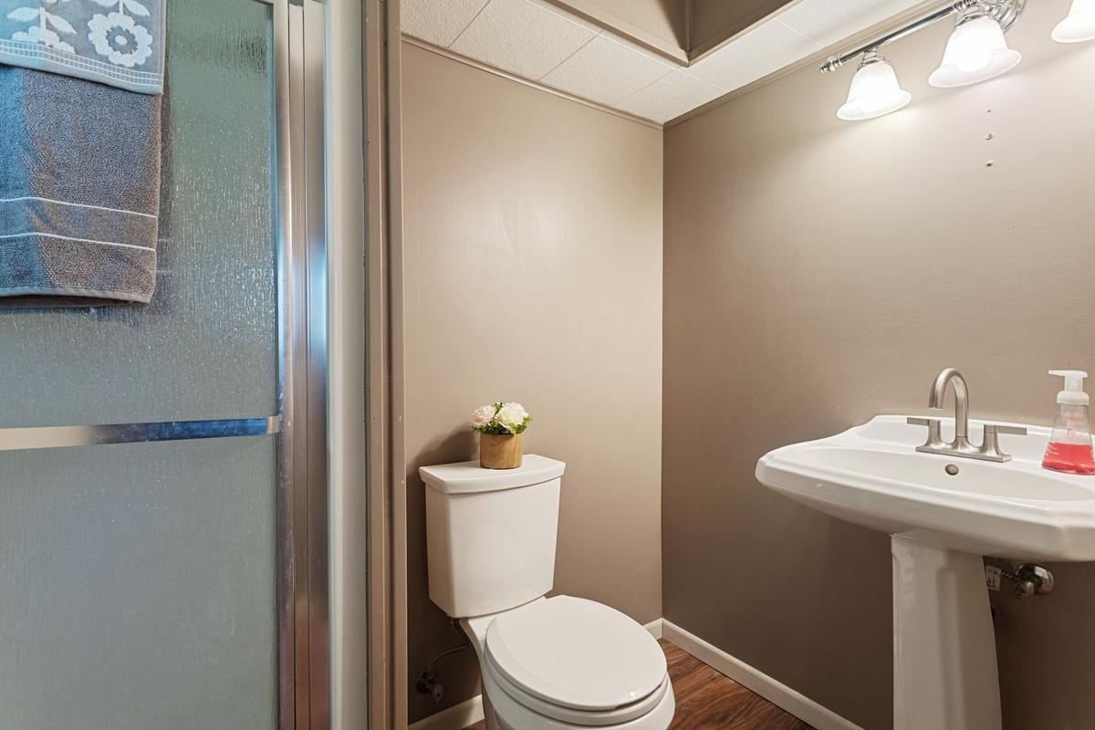 The lower-level three quarter bathroom features plank flooring for a clean, updated feel. The shower has a glass door . The charming pedestal sink completes the space, offering both style and functionality. This is an ensuite bathroom.