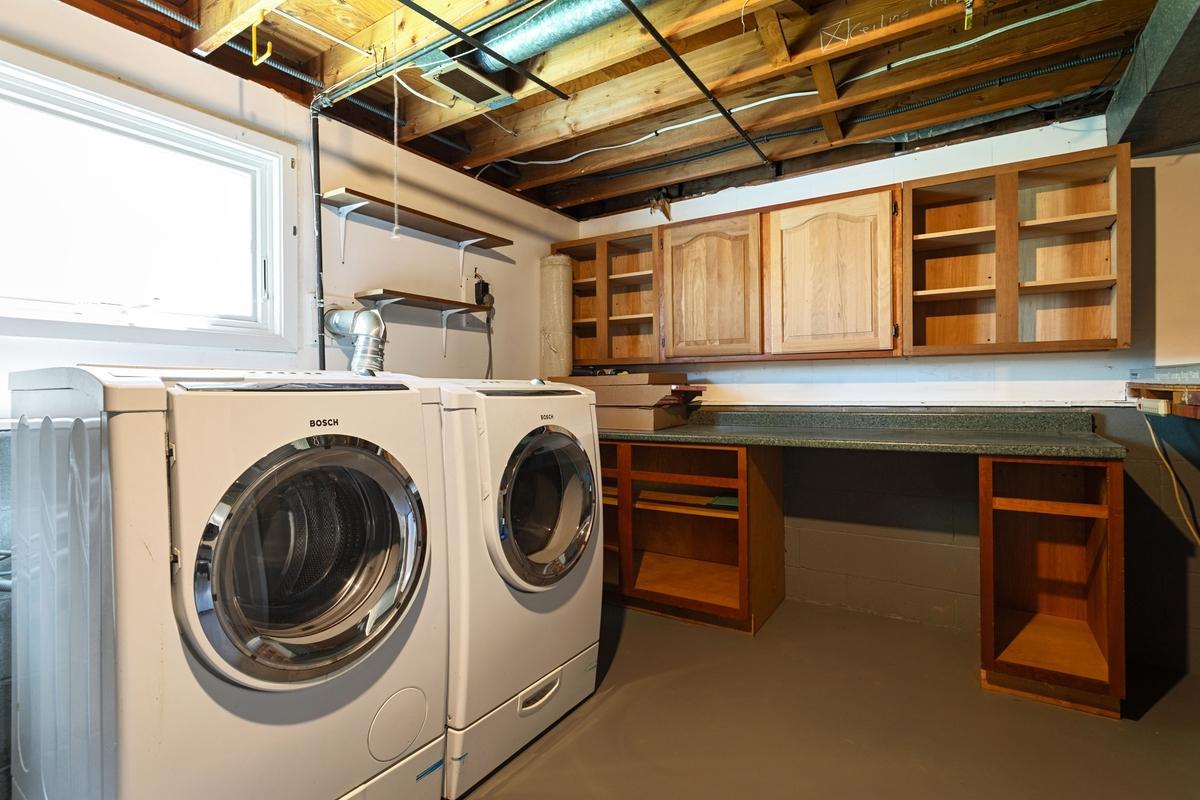 Functional utility room featuring a front-load Bosch washer and dryer set. New Furnace & AC (2021). The space offers ample cabinet and generous countertop workspace, making laundry tasks efficient and organized.