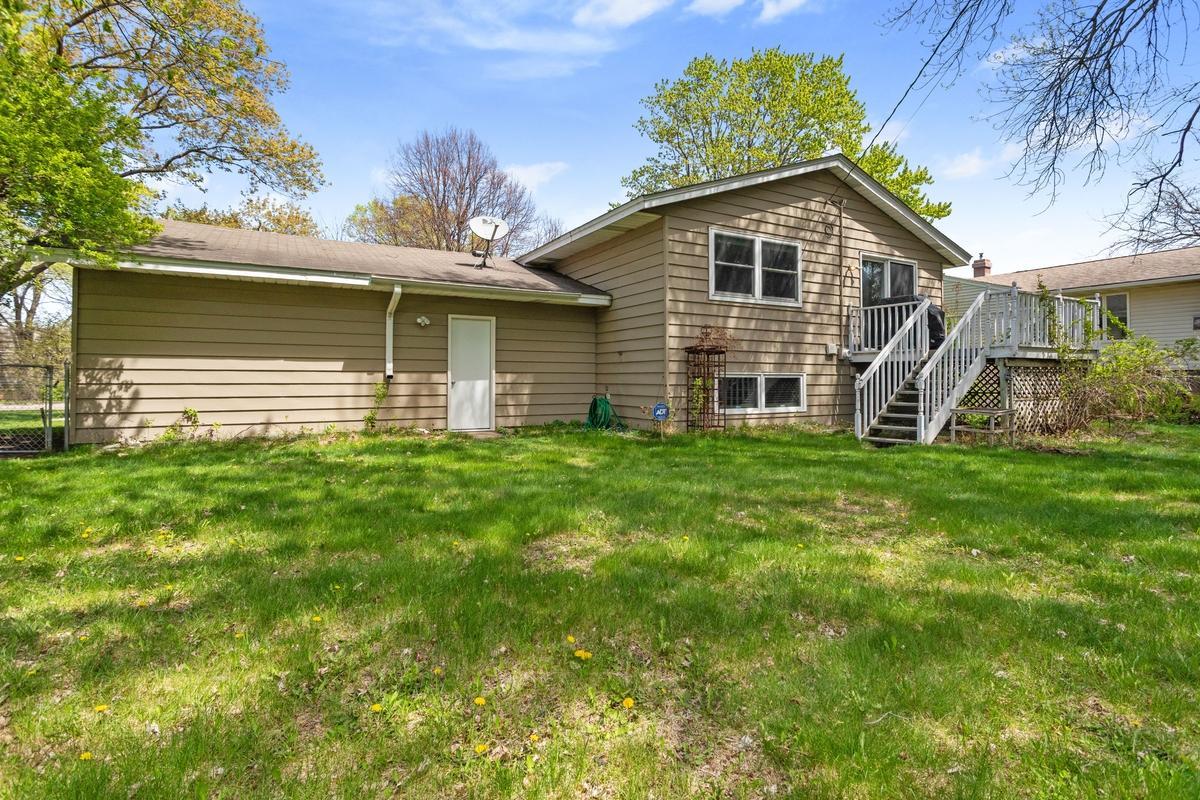 Rear exterior view of the home with deck & gas barbecue, perfect for outdoor entertaining. A new garage service door for convenience. The large, fully fenced yard is framed by mature trees, offering privacy, shade and a peaceful outdoor setting.