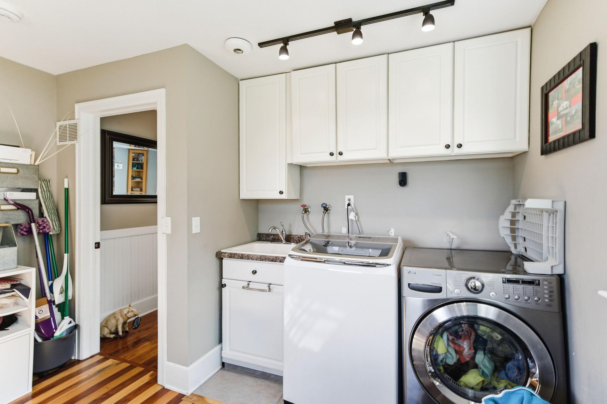 Functional Laundry setup with utility sink, cabinet storage, and overhead lighting.