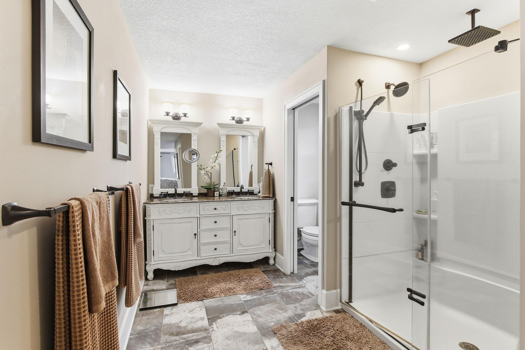 Updated private bath with dual sinks, tiled floors, and walk-in shower.