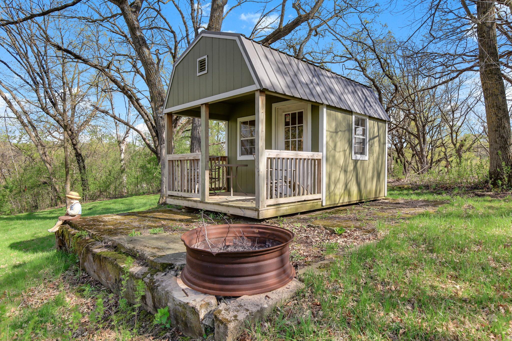 Charming Shed with covered front porch—perfect for relaxing, a playhouse, or a quiet retreat overlooking the yard.