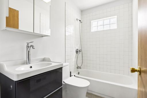 Renovated in 2020 - main floor full bath with tile shower surround and flooring, floating vanity, and glass block window.