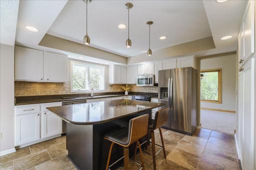 Kitchen features newly enameled cabinetry w/undermount lighting, quartz countertops w/ tile backsplash, stainless steel appliances, travertine tile flooring and combination of recessed and pendant lighting.