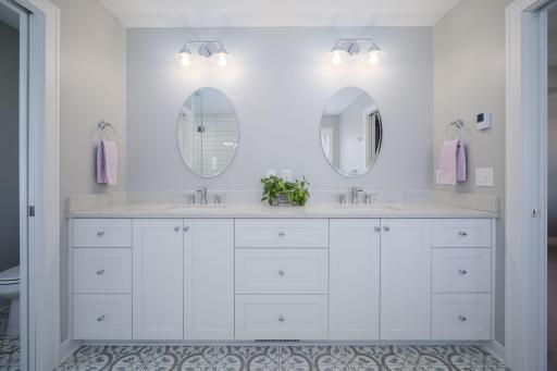 His and hers done right. A generous double vanity with crisp white cabinetry, stone countertops, and warm mirror lighting that makes getting ready feel like a luxury