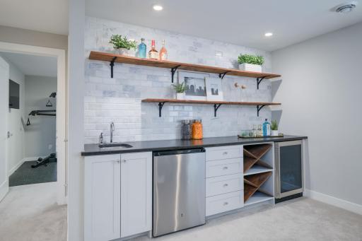 Pour one for the host. The custom wet bar features a wine rack, beverage fridge, bar sink, and a warm open shelving that makes entertaining downstairs feel effortless and elevated.