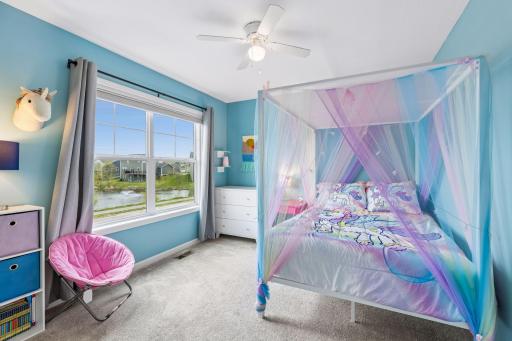 Bright upper level bedroom with large window, ceiling fan, and peaceful pond views.