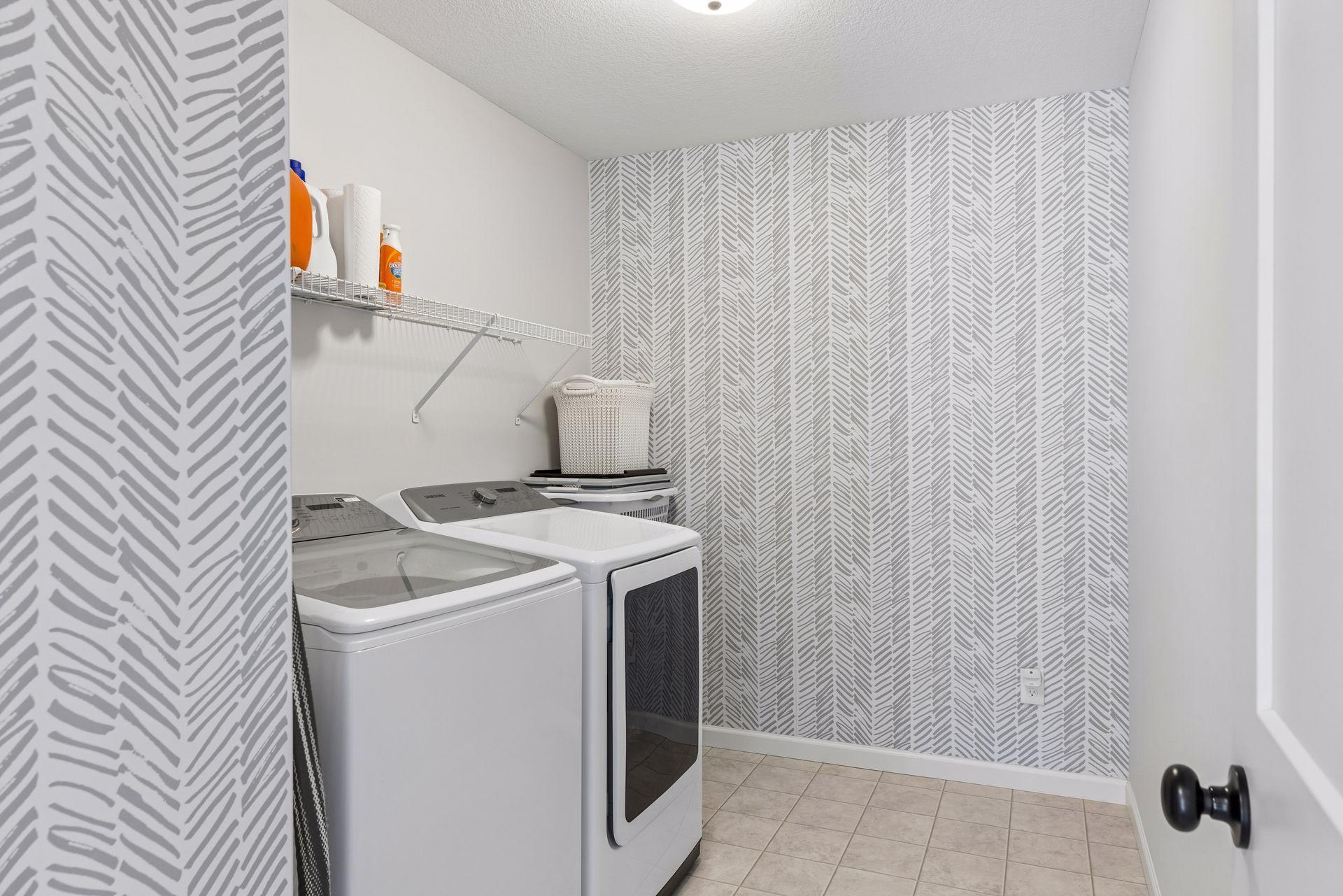 Convenient upper level laundry room with additional storage space and stylish accent wallpaper.