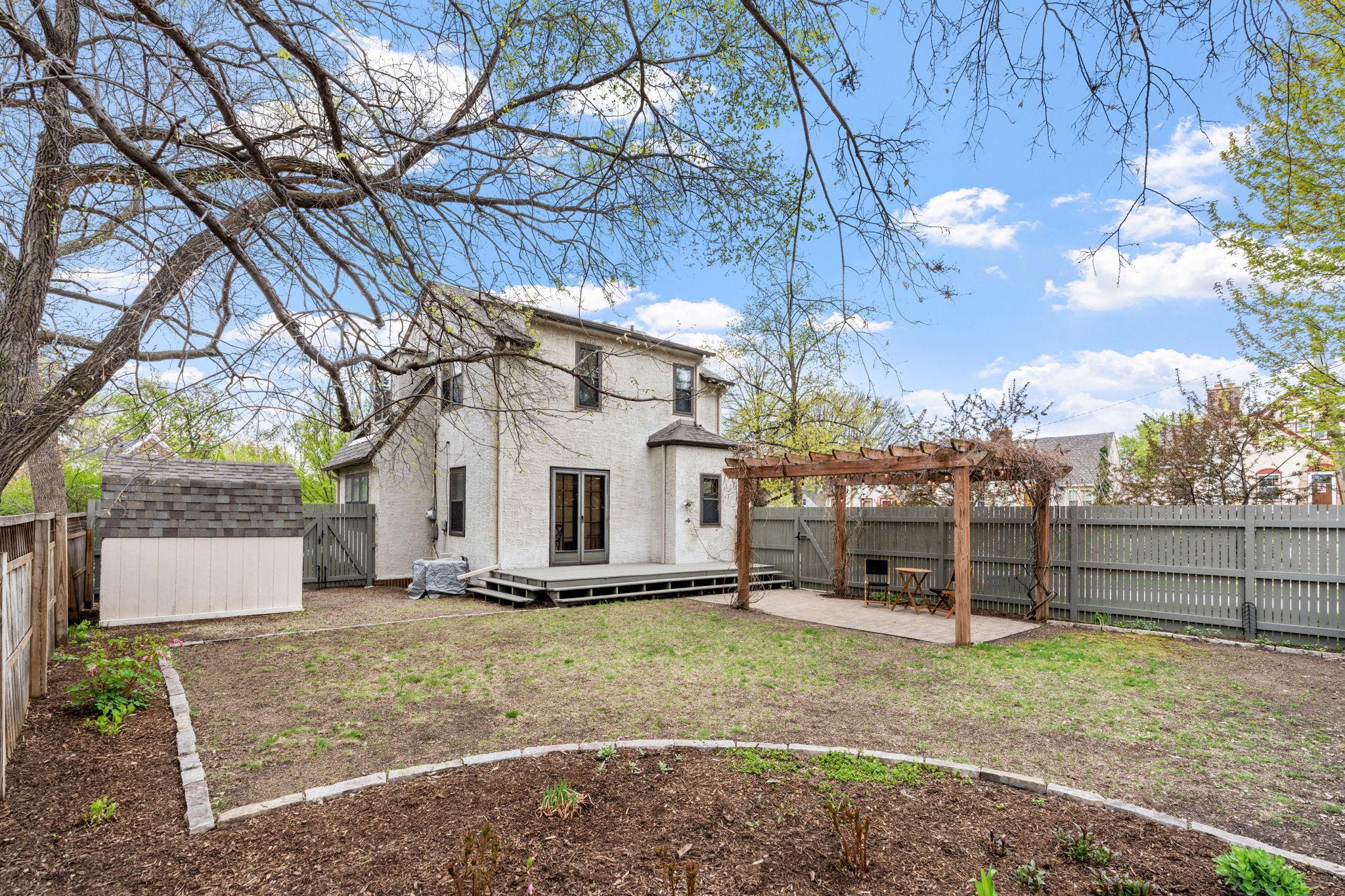 Beautiful outdoor living featuring a deck, privacy fence, charming vine-draped pergola, and lush landscaping!