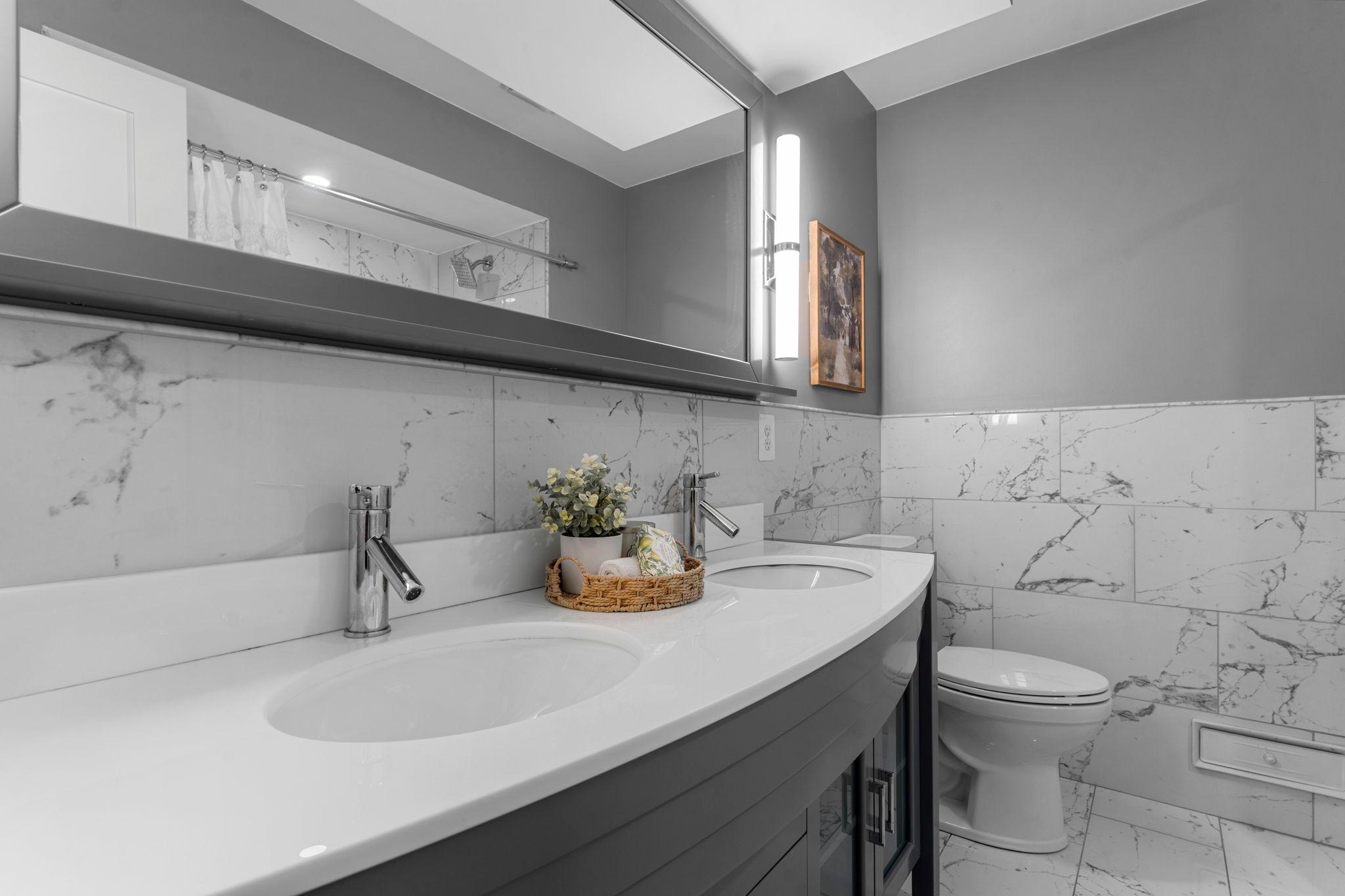 The centrally-located full bathroom (updated in 2021) feels like a spa, featuring a tiled tub/shower combo, jetted soaking tub, double vanity, tile flooring and wainscoting, dimmable lighting, and a hall closet for extra storage.