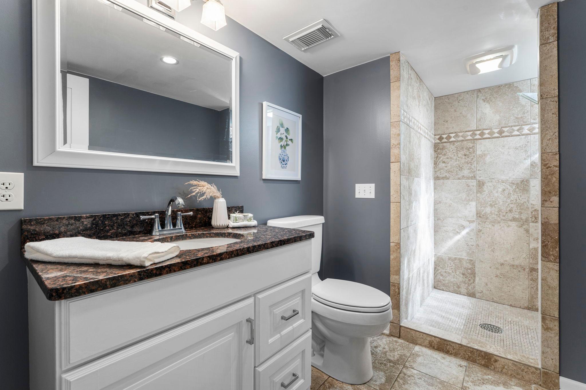 Convenient 3/4 bathroom with a walk-in tiled shower, along with vanity for storage.