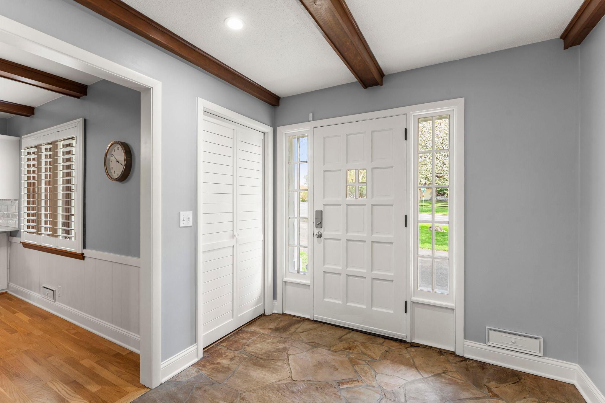 The level is completed by a spacious entryway with stone flooring, wood beam ceiling detail, and a large closet for seasonal storage. Direct main-level access leads to the heated, attached, 2-car garage with shelving and additional storage space.