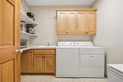 Large main-floor laundry room conveniently located between the kitchen and garage, featuring ample storage, shelving, and truly a dream laundry space