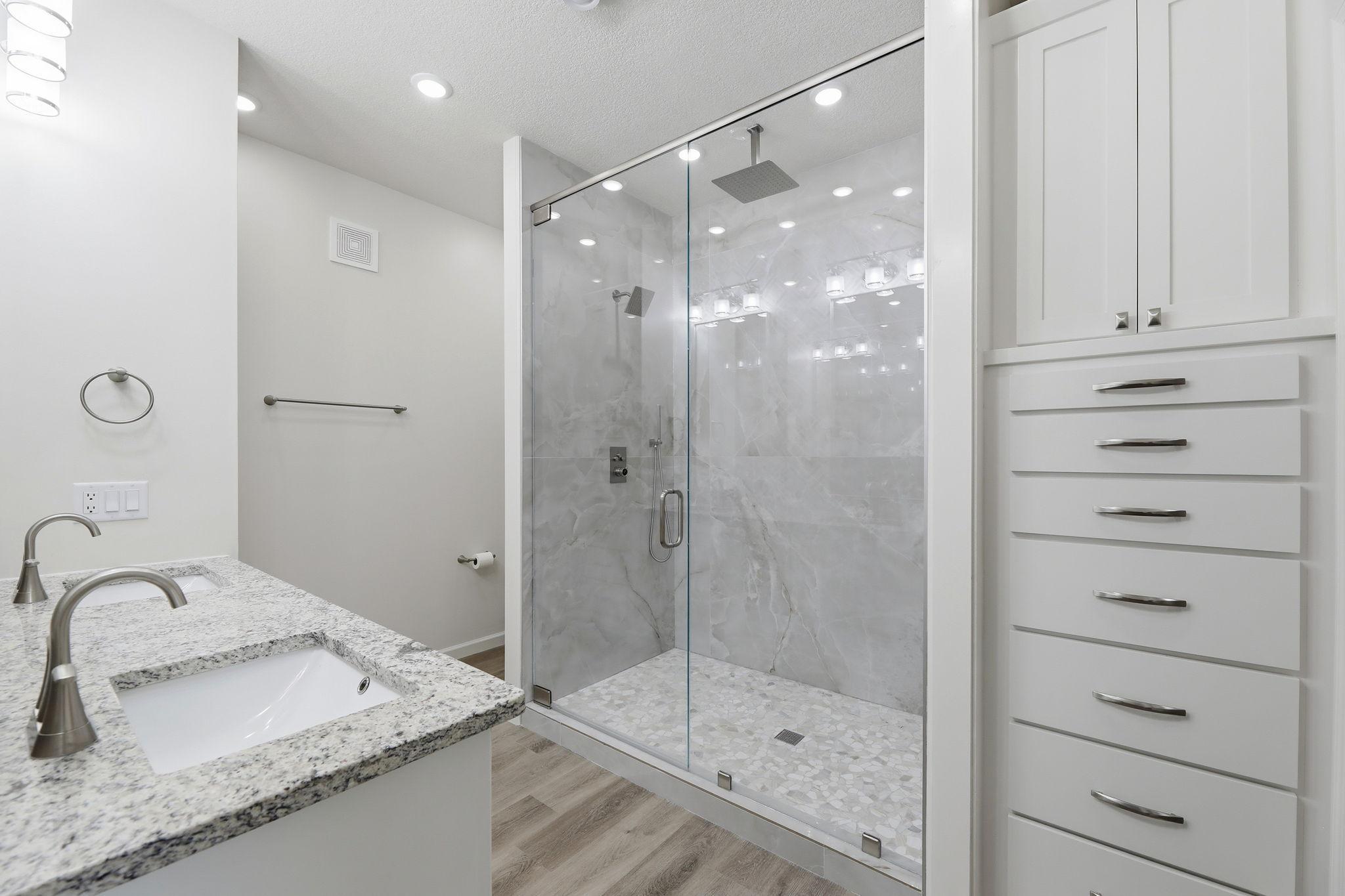 Elegant tiled walk-in shower featuring two tall banks of additional cabinets and drawers for exceptional storage