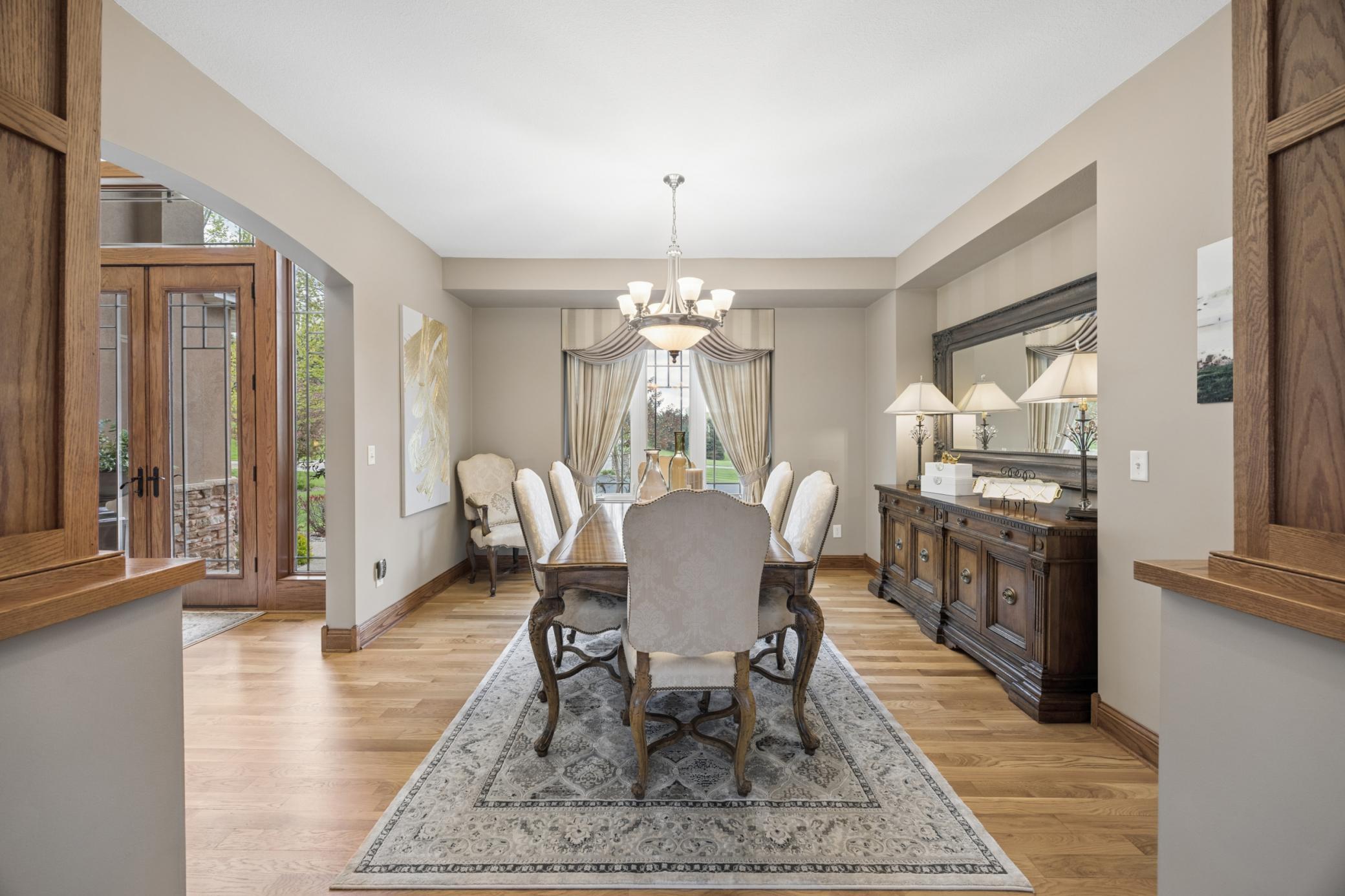 Elegant formal dining room featuring rich hardwood floors, classic millwork perfectly complemented by large windows and custom drapery.