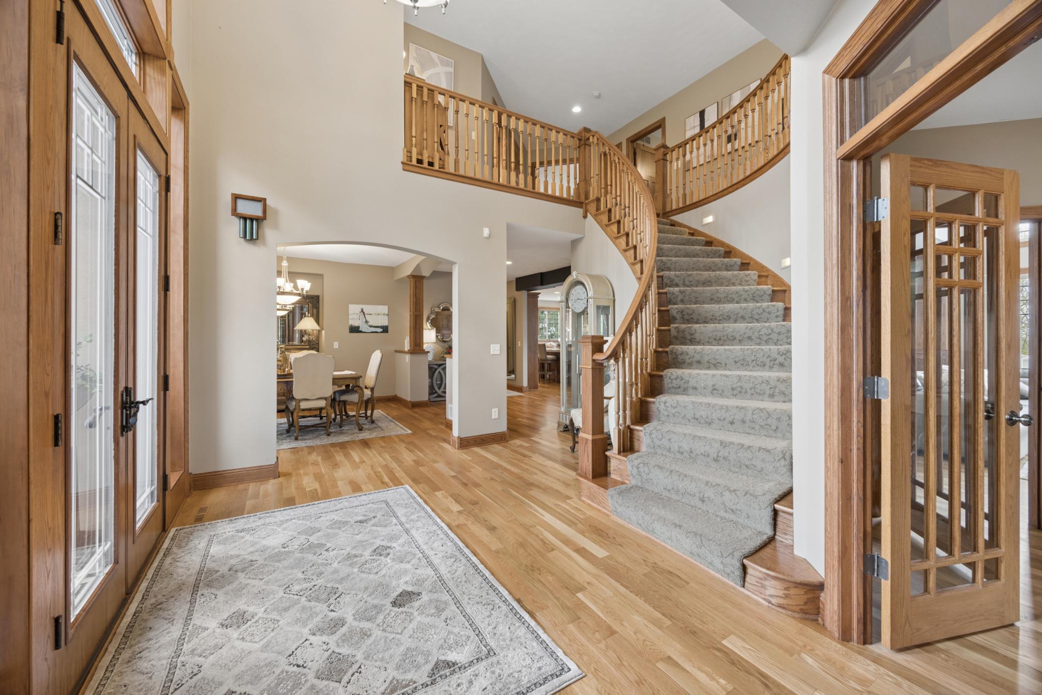 Dramatic foyer showcasing a sweeping staircase, warm wood tones, and sun-filled spaces that set a refined tone from the moment you enter.