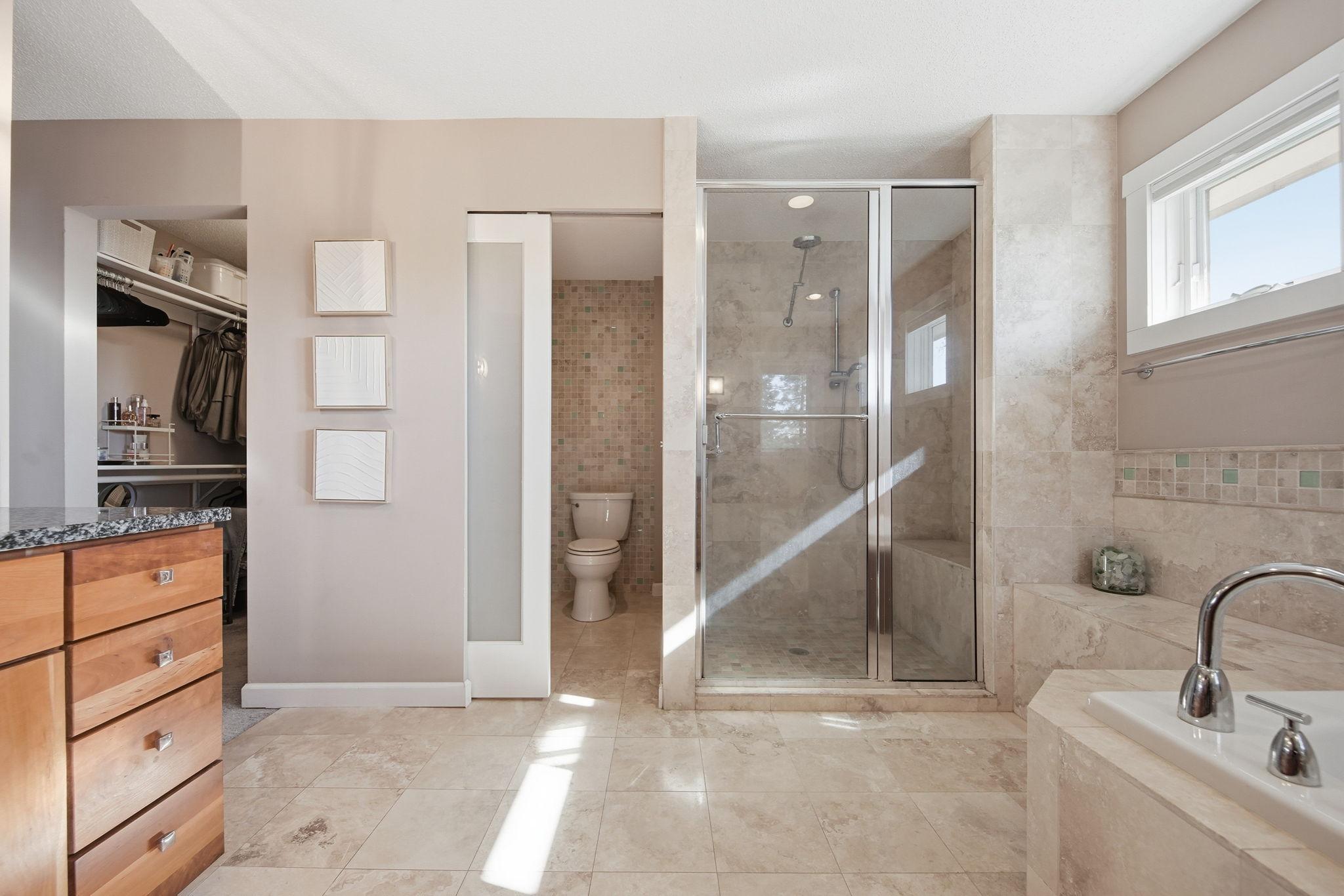 Custom Travertine walk-in shower has bench, body sprays dual showerheads and a rainfall showerhead