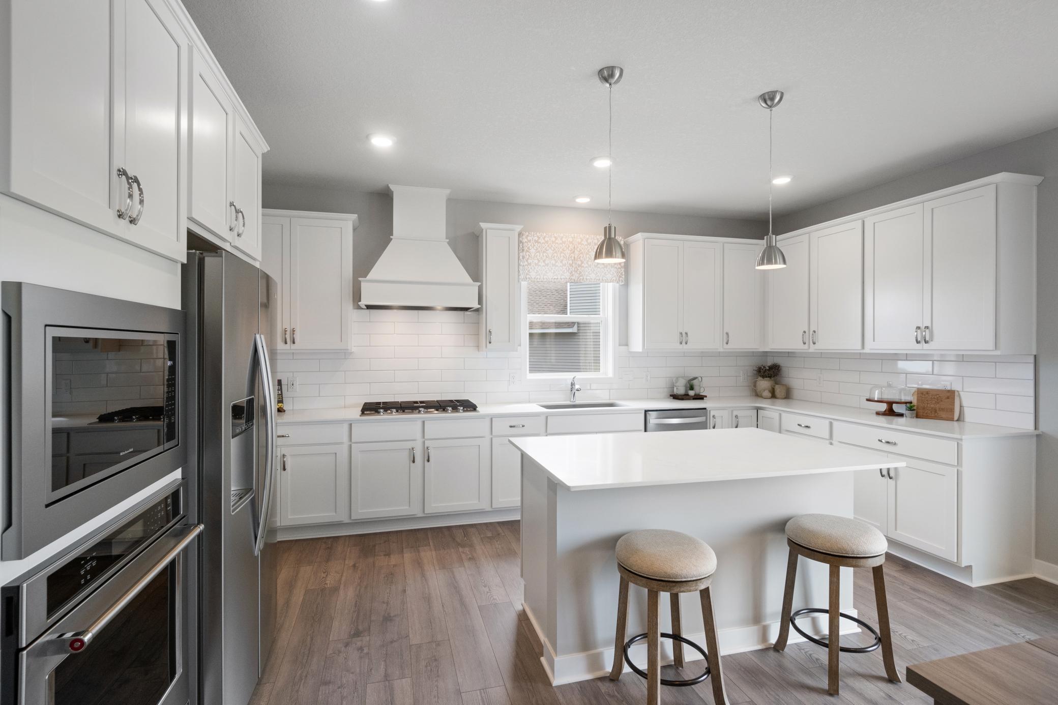Welcome to your gourmet kitchen, complete with gas cooktop, wood hood vent, tile backsplash, and center island. Photo of model, colors and finishes may vary.