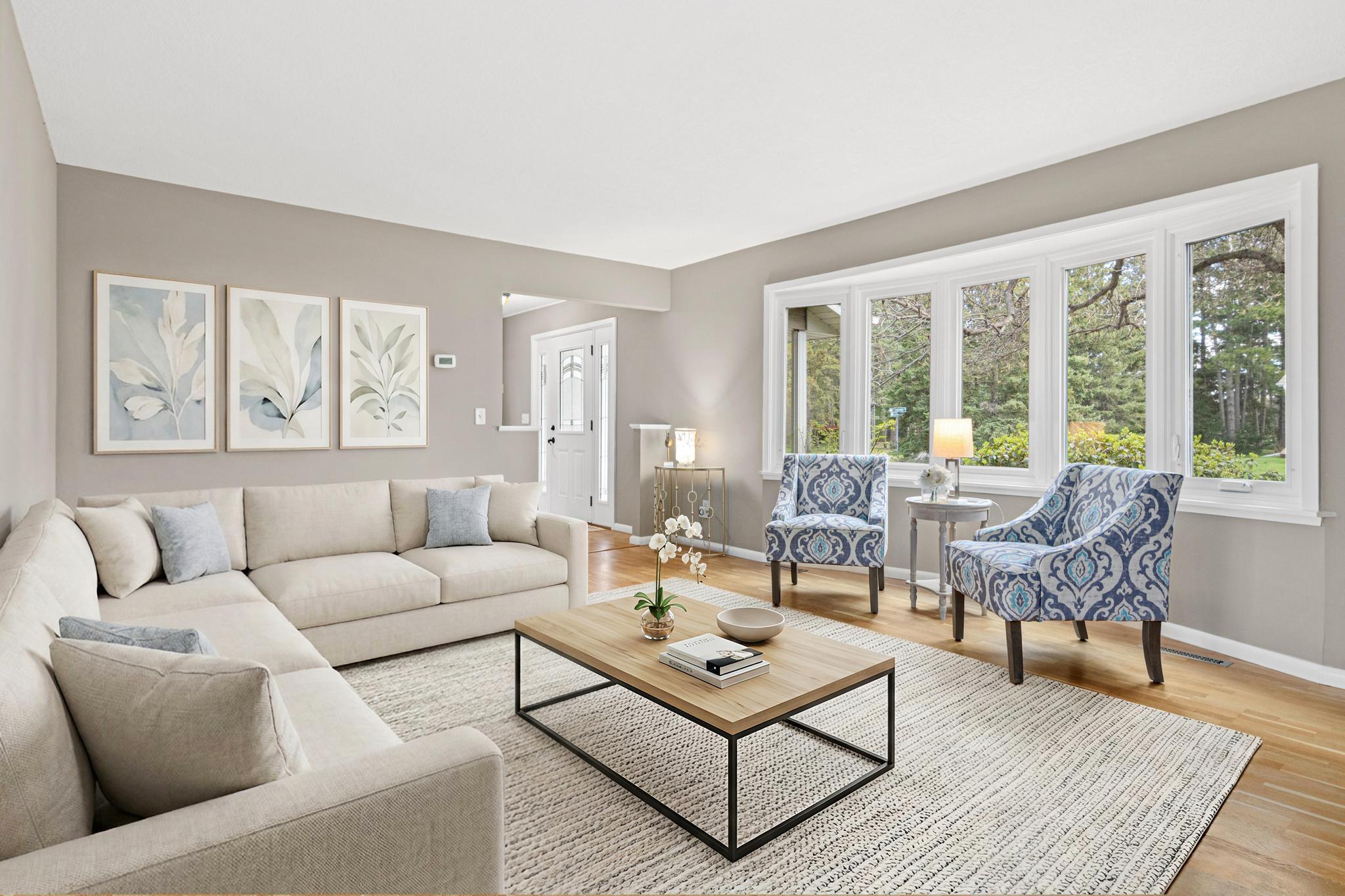 Formal living room filled with natural light and expansive windows. Visually staged.