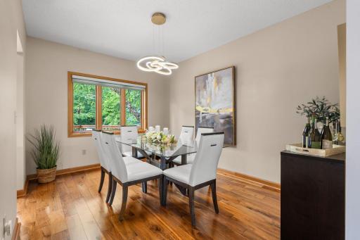 Elegant formal dining room featuring gorgeous wood floors, a modern light fixture, and a large window.