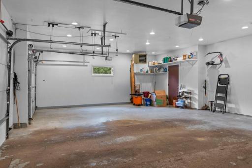 Garage interior features a dedicated recessed lighting, overhead heater, built-in shelving, and direct service door access to the home.