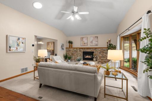 Expansive living room boasting vaulted ceilings, a cozy stone-surround fireplace, and large sun-filled windows.