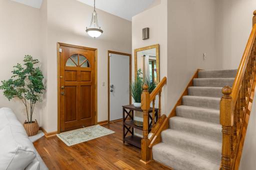 Bright foyer entry featuring warm wood floors, a classic timber staircase, and direct garage access.