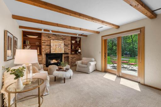 Cozy lower-level family room highlighted by exposed ceiling beams, a brick fireplace, and sliding doors to the patio.