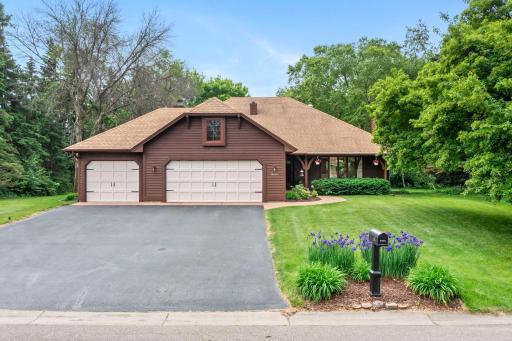 Classic cedar-sided exterior featuring an attached 3-car garage and vibrant perennial landscaping.