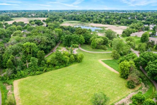 Broad aerial overview highlighting the home's proximity to sprawling neighborhood greenways, a local park playground, and a scenic pond.