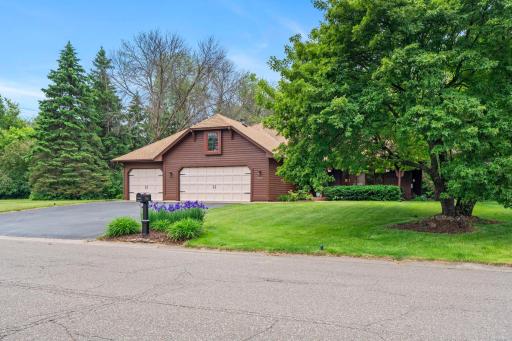 Welcoming street view showcasing the mature trees, manicured lawn, and expansive asphalt driveway.