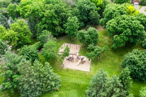Bird's-eye view of a beautifully maintained neighborhood playground, perfectly nestled among lush, mature greenery. Close proximity from the trail behind the house