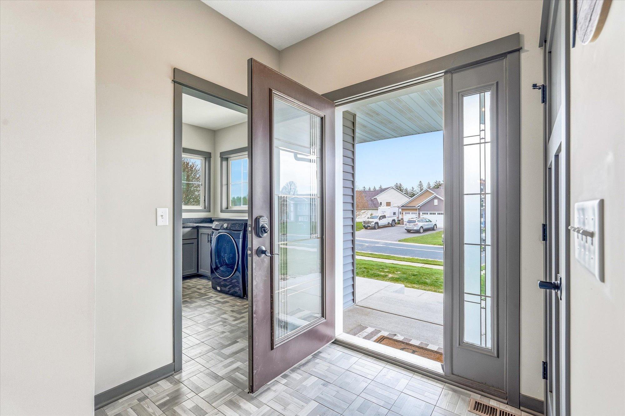 Bright and welcoming foyer with stylish tile flooring, tall ceilings, and modern gray trim and doors throughout. Front entry showcases beautiful natural light and easy access to the spacious laundry and mudroom area.