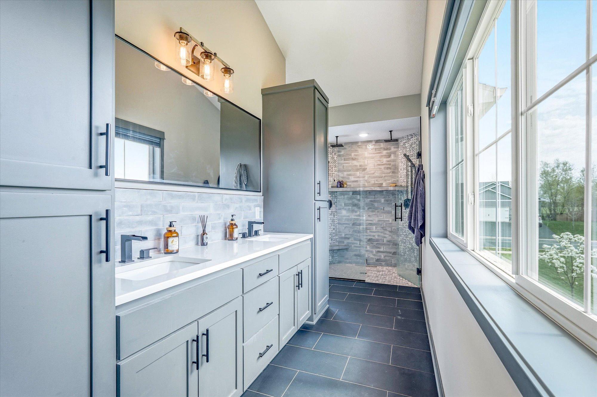 Luxurious primary bathroom featuring dual vanities, quartz countertops, custom cabinetry, and a beautifully tiled walk-in shower.