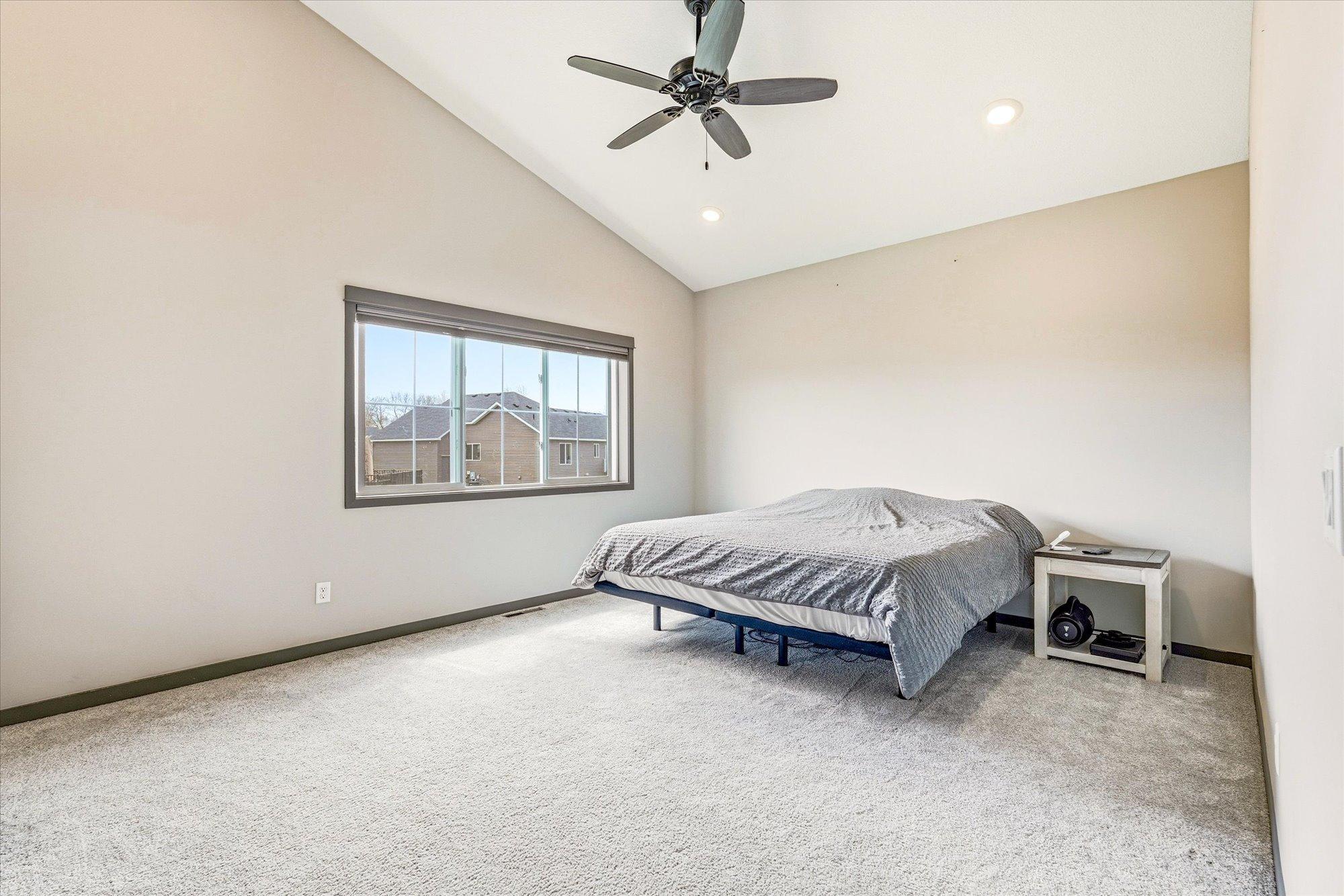 Spacious primary bedroom with vaulted ceilings, plush carpet, ceiling fan, and oversized window for great natural light.