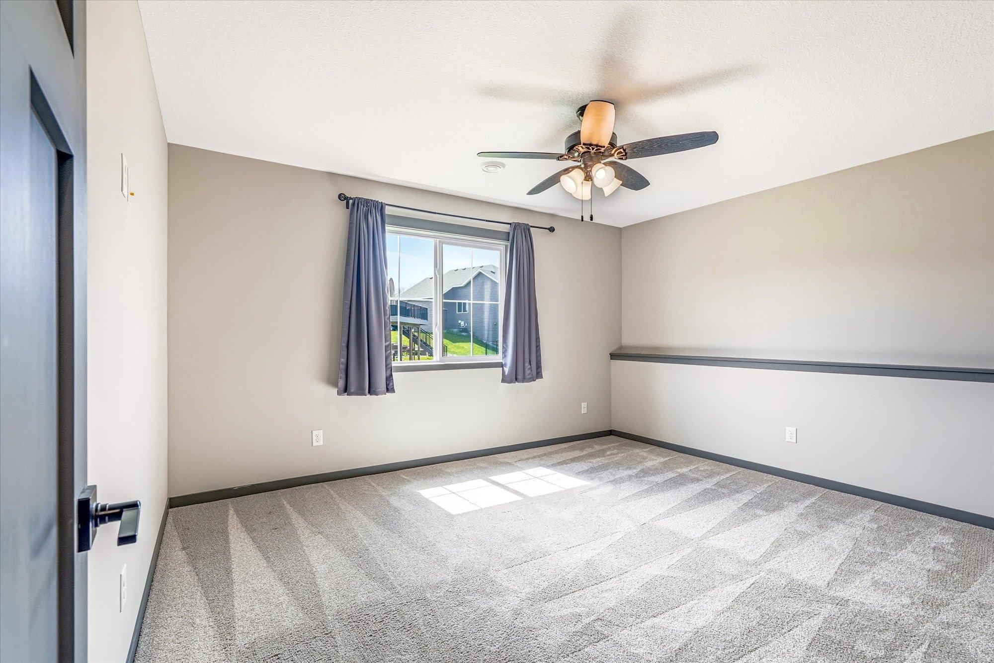 Spacious lower-level bedroom with plush carpet, large window, and neutral finishes creates a comfortable guest or family retreat.