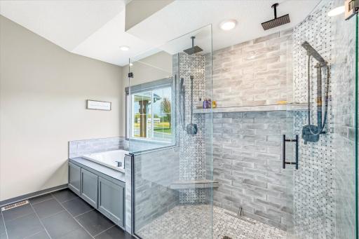 Spa-like primary bathroom features a stunning walk-in tiled shower with dual shower heads, bench seating, and sleek glass surround.