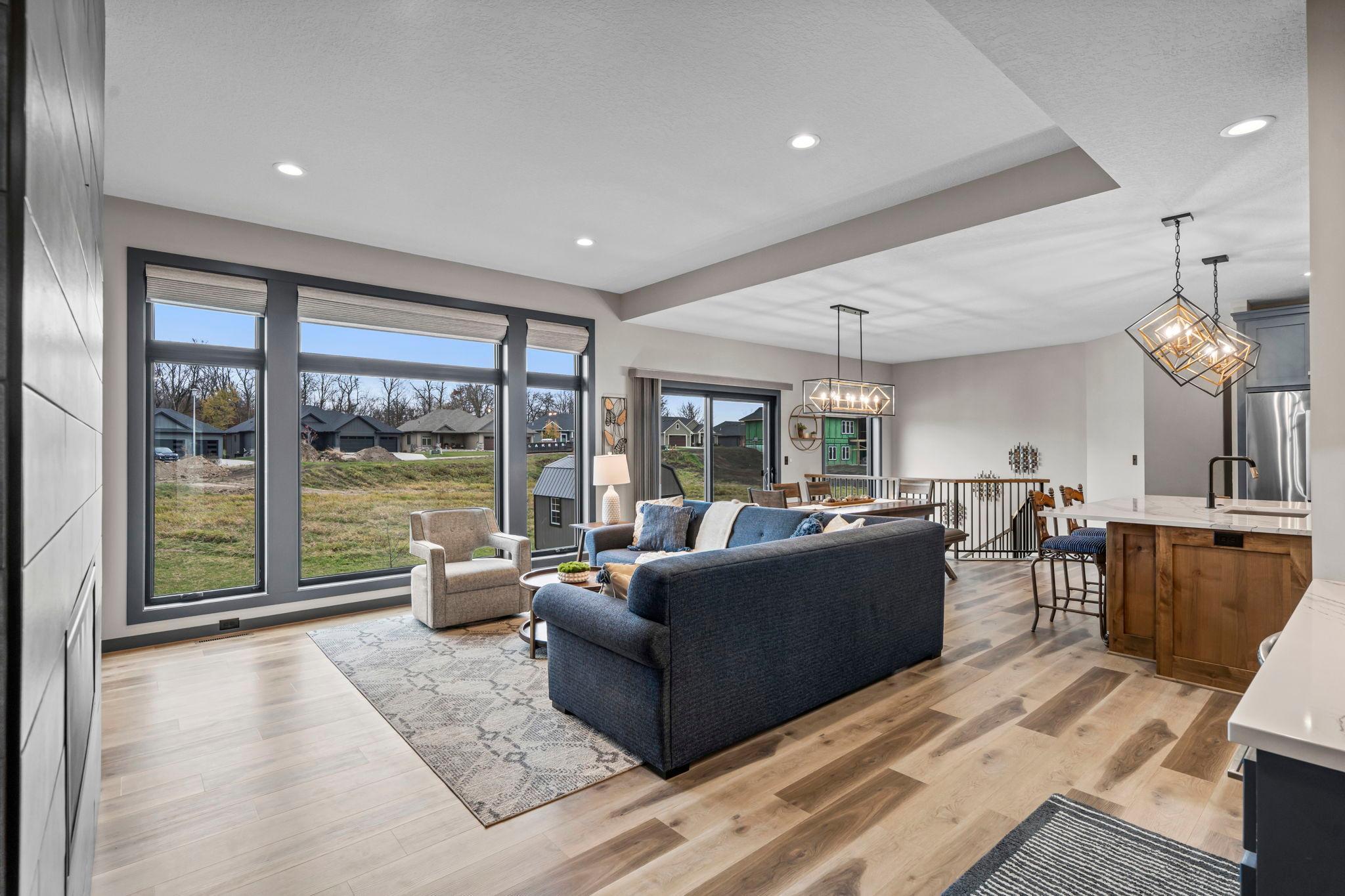 Sunlight pours into the open living room through walls of windows, highlighting the gorgeous plank wood floors