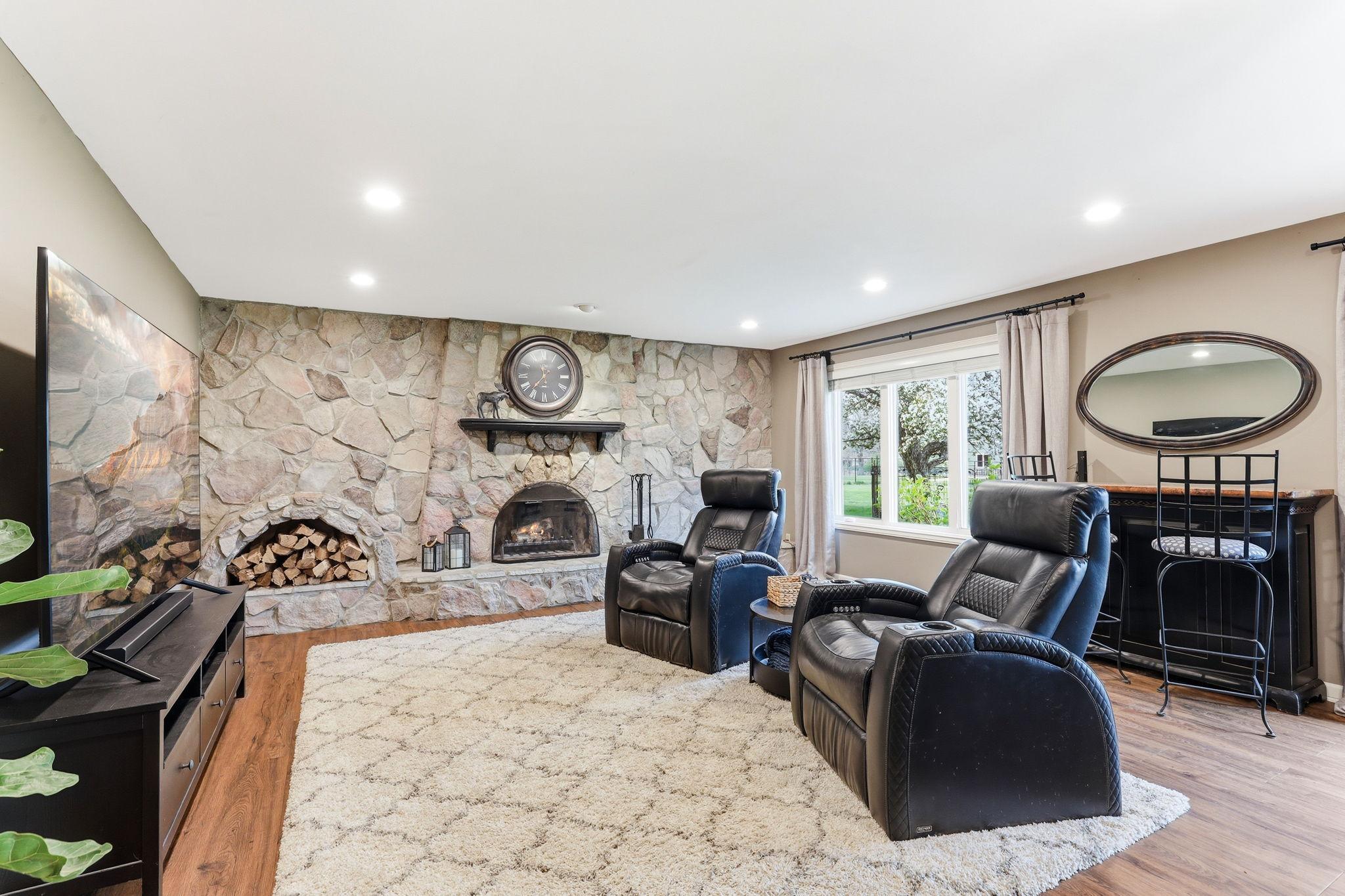 The lower-level family room offers a warm and inviting retreat, highlighted by a stunning full-height stone wall and a classic wood-burning fireplace.