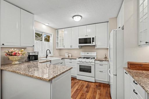 The fresh and Bright Kitchen features stone countertops, farm sink, wood floors and openness to dining and living room.