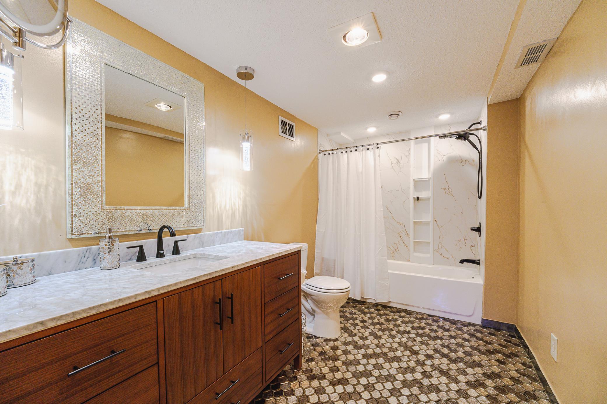 The first bedroom has a glamorous, REMODELED, FULL ENSUITE BATH with glittering arabesque tile flooring, Kohler panels in the tub, a new vanity, new fixtures, a heat lamp, and fashionable lighting.
