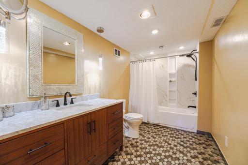 The first bedroom has a glamorous, REMODELED, FULL ENSUITE BATH with glittering arabesque tile flooring, Kohler panels in the tub, a new vanity, new fixtures, a heat lamp, and fashionable lighting.