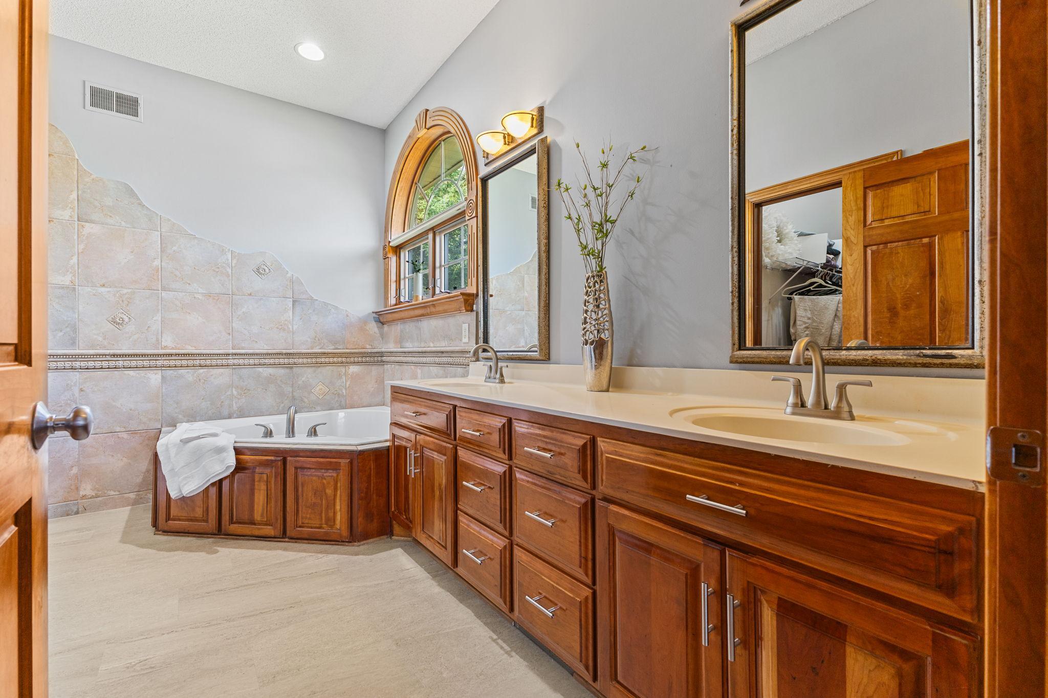 Private primary bath features a jetted soaking tub, new LVP floors (2026), and dual vanities plus walk in closet access allowing for a comfortable reset each morning.
