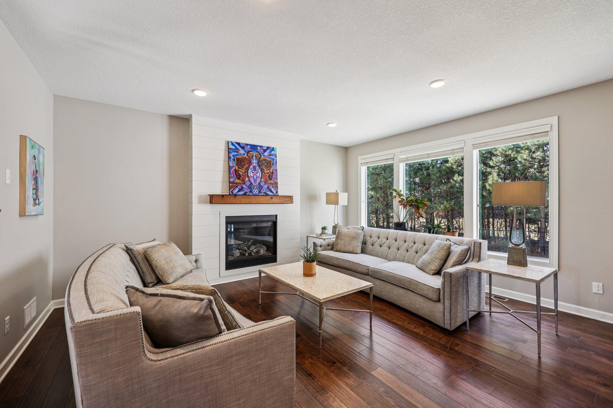 Bright main level living room featuring hardwood floors, gas fireplace with shiplap surround, and open sight-lines to the entry and staircase.