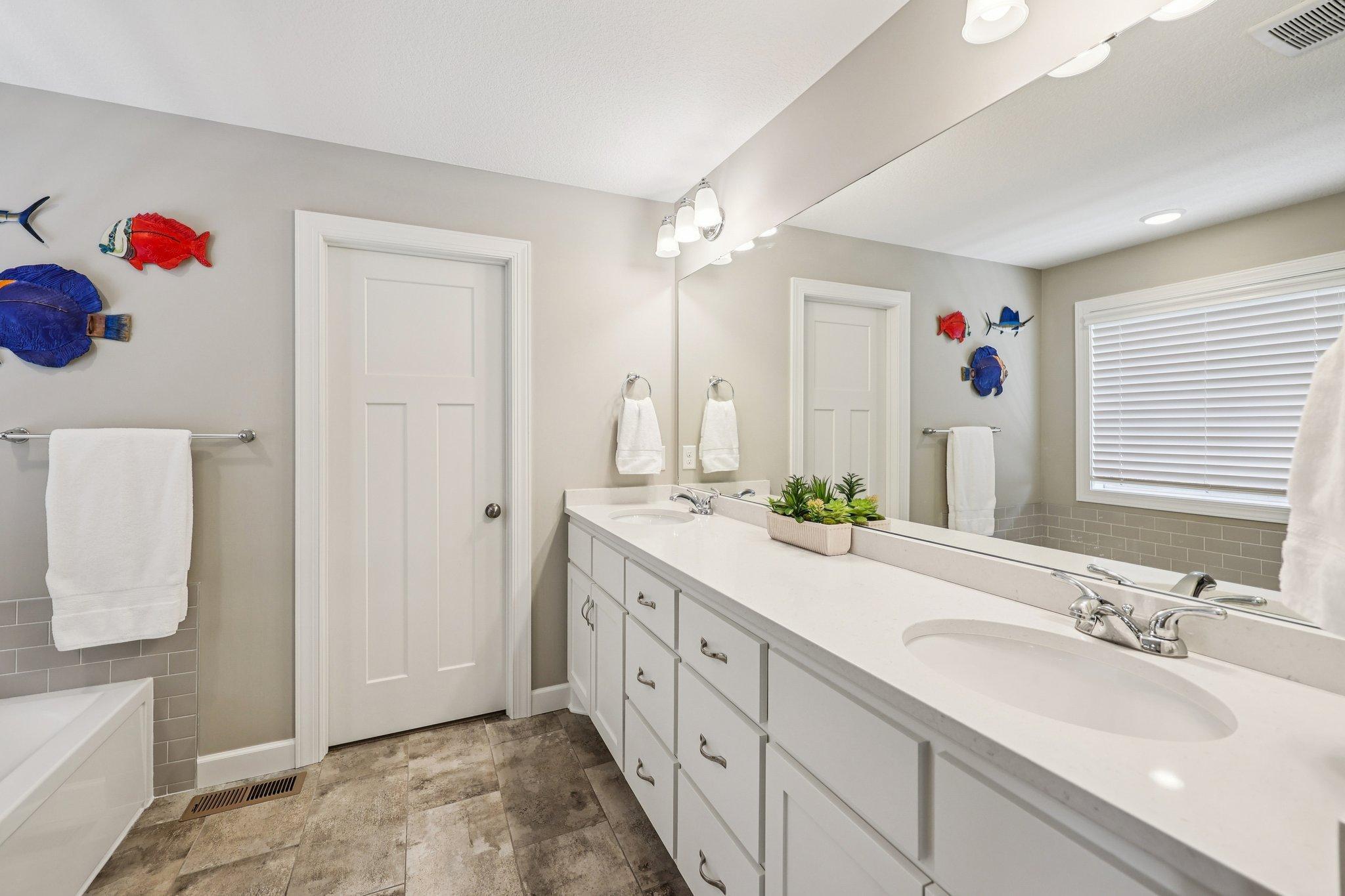 Spacious owner’s bath with double vanity, tiled flooring, soaking tub, separate shower, and generous storage.
