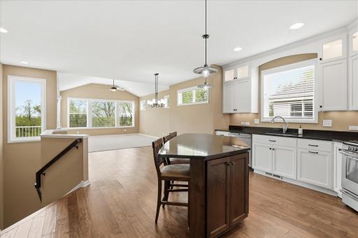 Looking across the kitchen center island with the hardwood floors extending thru the dining room, then vaulted and carpeted great room. To the left are stairs to the lower level