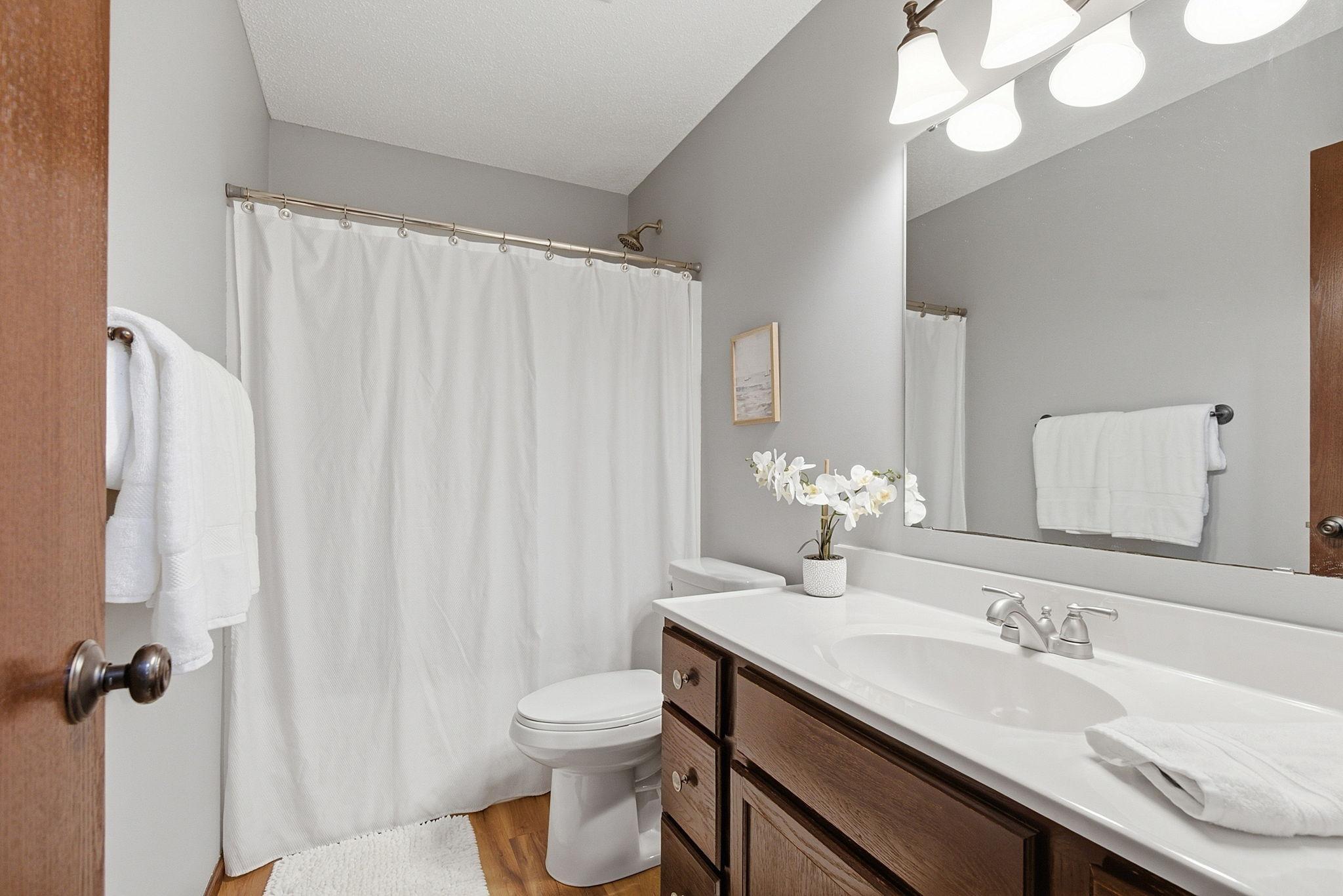 Clean and inviting bathroom featuring a large vanity, bright lighting, and a full tub with shower.