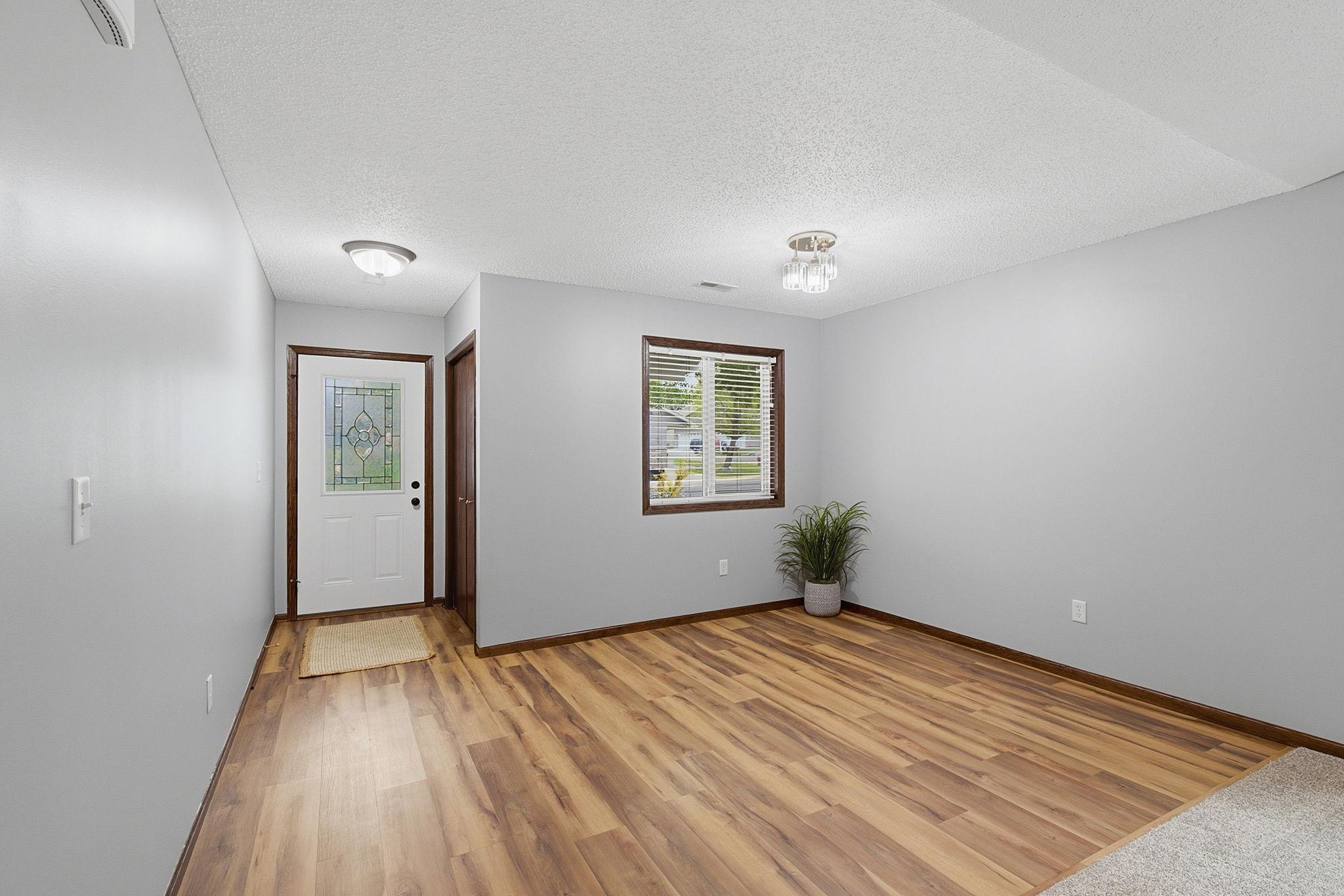 Bright entryway with wood-look flooring, decorative glass front door, and a large window bringing in natural light.