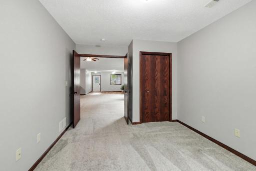 Comfortable carpeted bedroom with neutral walls, rich wood trim, and double doors opening to a bright adjoining living area.