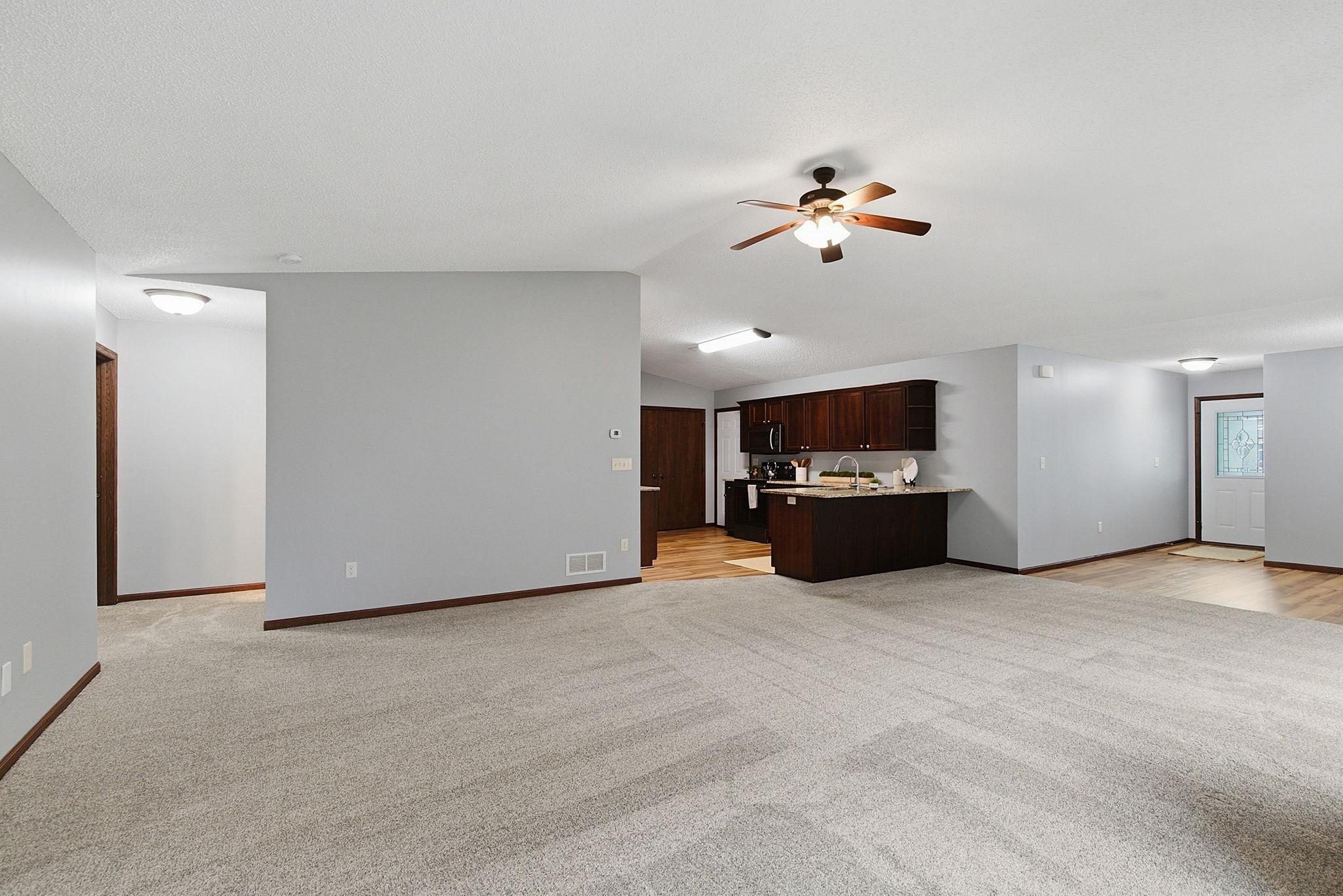 Open-concept living and dining area with plush carpeting, a modern kitchen with dark wood cabinetry, and warm overhead lighting.